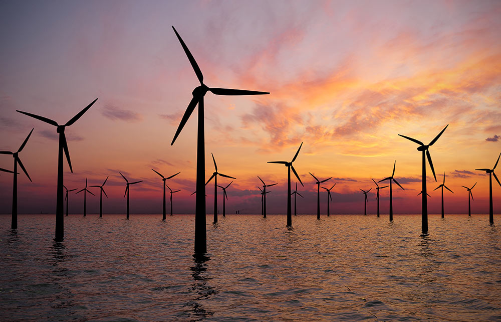 This is a picture of wind turbines in a wind farm. It is sunrise as the wind turbines are in a body of water.