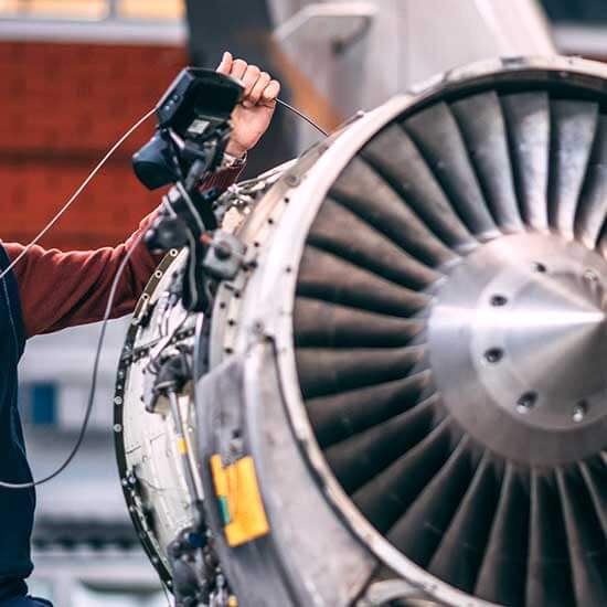 A technician inserts a device into a jet engine to analyze the reliability, previous maintenance, and engine life